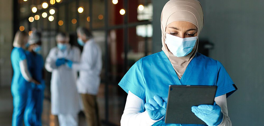 Healthcare professional in scrubs, mask and gloves using iPad
