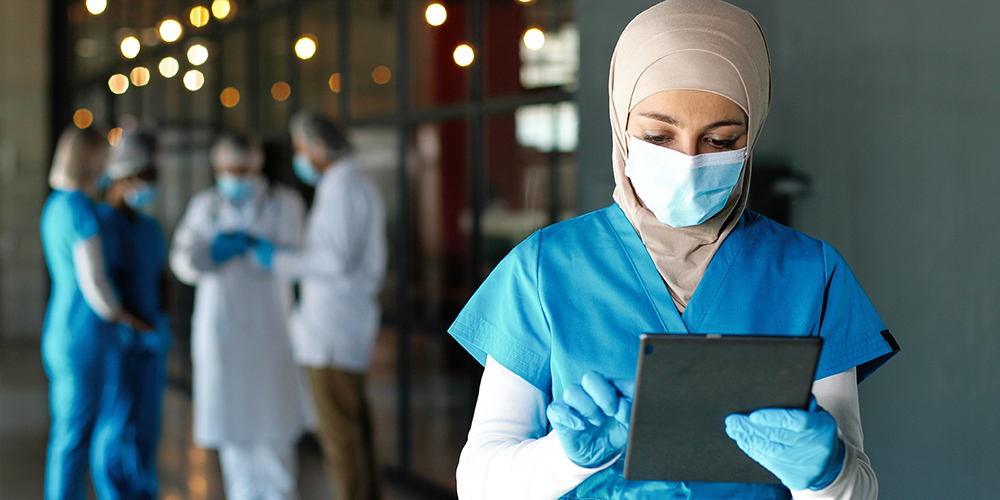Healthcare professional in scrubs, mask and gloves using iPad