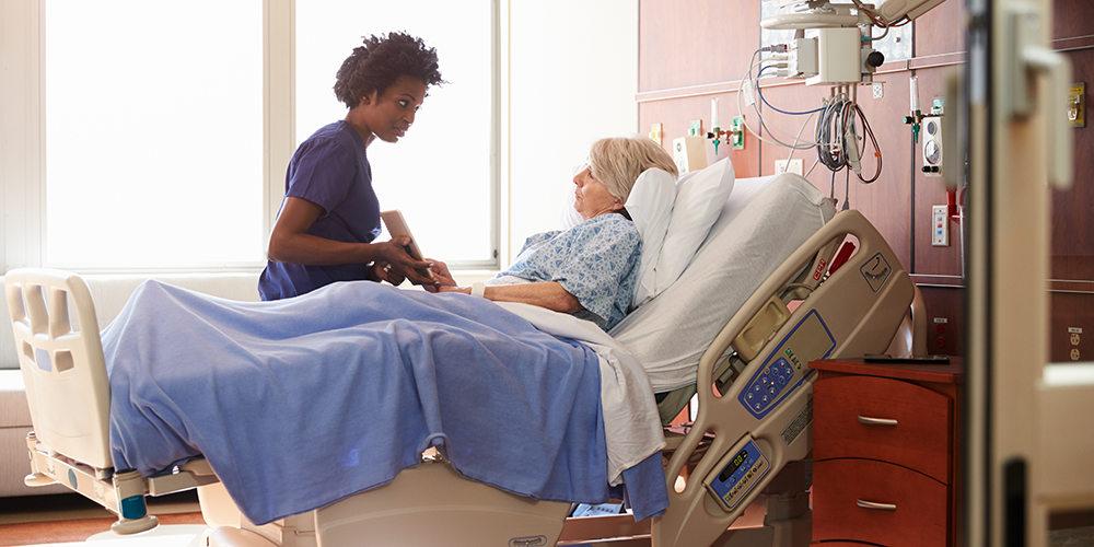 Nurse talking to elderly lady patient in bed