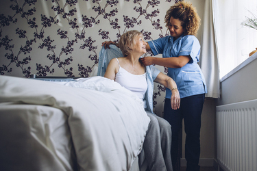 Home Caregiver helping a senior woman get dressed in her bedroom.